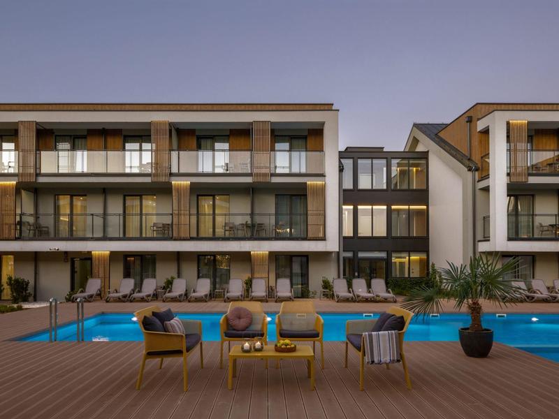 Nowoczesny hotel z basenem, leżakami i miejscem do siedzenia na tarasie o zmierzchu.