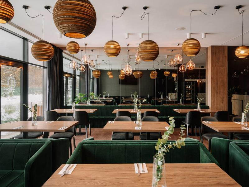 Nowoczesne wnętrze restauracji z zielonymi boksami i wiszącymi drewnianymi lampami.