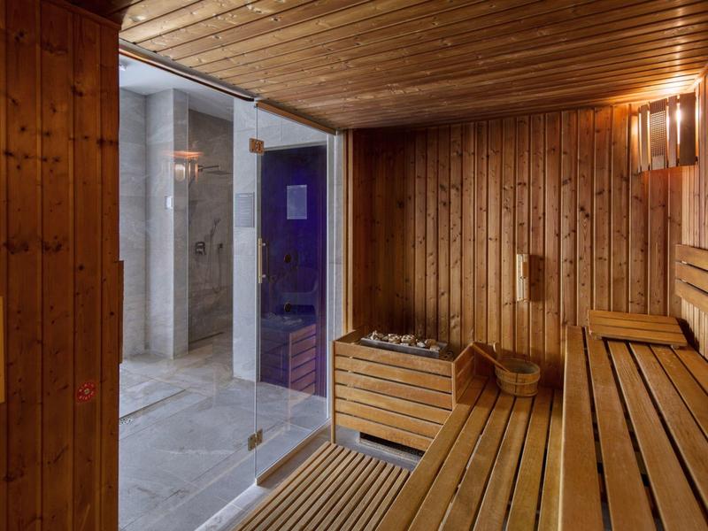 Pomieszczenie sauny z drewnianą boazerią, ławkami i szklanymi drzwiami do prysznica