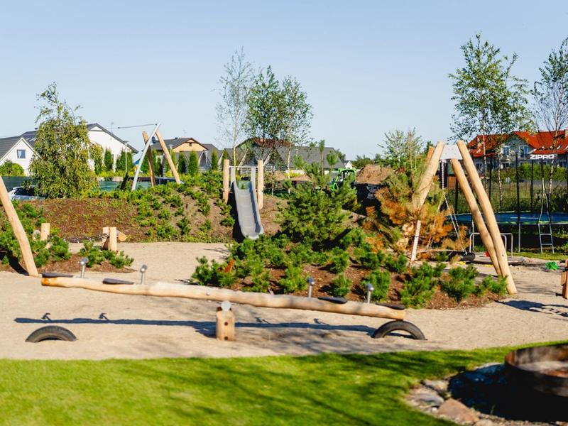 Plac zabaw z drabinką do wspinaczki, huśtawkami i piaskownicą na osiedlu mieszkaniowym w słoneczny dzień.