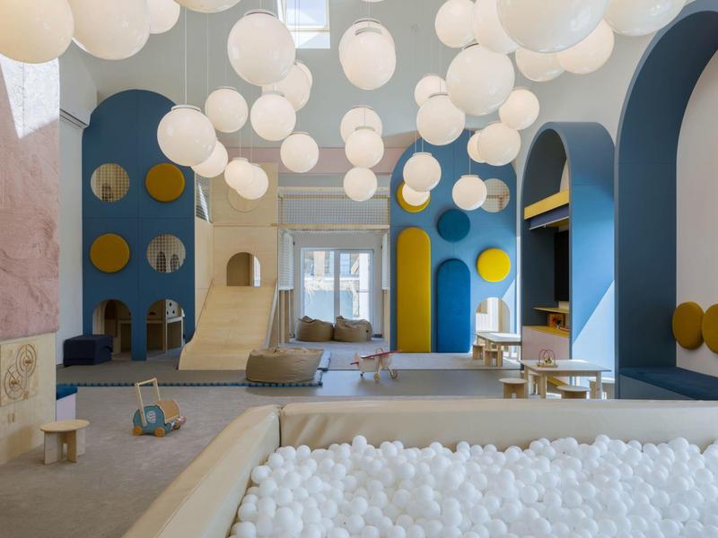 Nowoczesne wnętrze z wiszącymi kulistymi lampami, basenem z kulkami i zabawnymi elementami architektonicznymi.