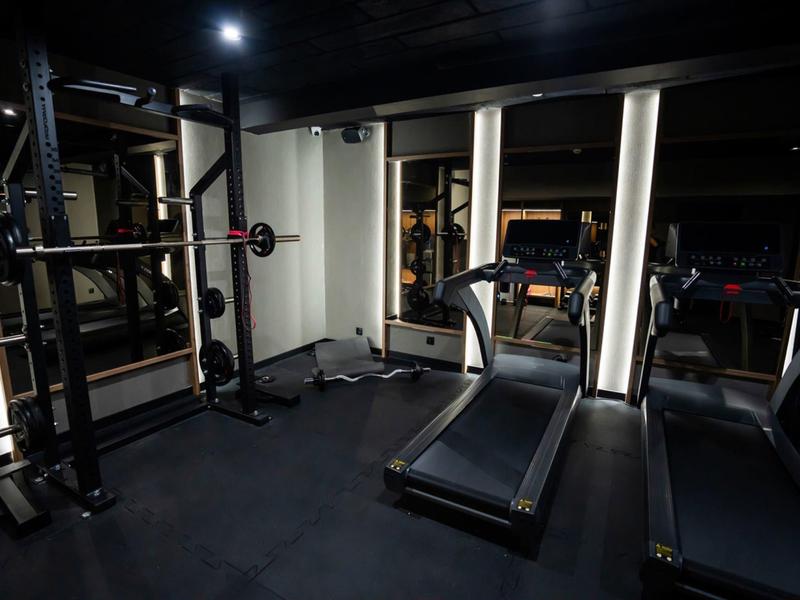 Słabo oświetlona siłownia z bieżnią i sprzętem do ćwiczeń siłowych.