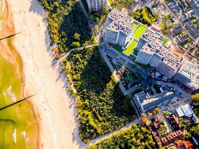 Letecký pohled na pláž vedle zalesněné oblasti a čtvrti s budovami.