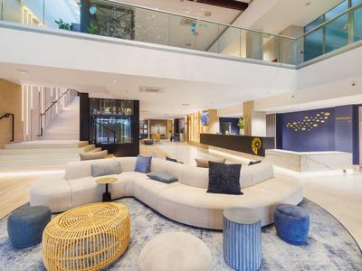 Moderna recepción de hotel con sofá blanco curvado y cojines sobre alfombra.