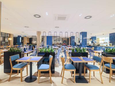 Restaurante moderno y luminoso con sillas azules y mesas de madera, decorado con plantas.