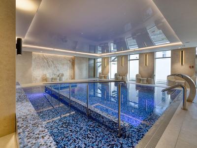 Moderní vnitřní bazén s mozaikovými dlaždicemi, nerezovým zábradlím a vodopádem v luxusní wellness zóně