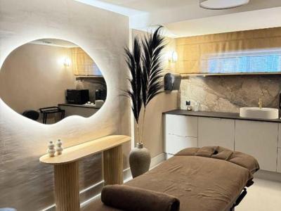 Moderní wellness místnost s masážním stolem, kulatým zrcadlem a stylovým osvětlením.