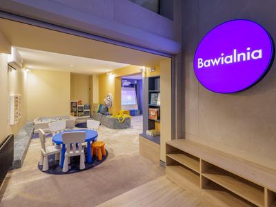 Světla herna pro děti s malými stoly, židlemi a hračkami v hotelové části.