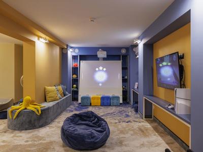 Moderní obývací prostor se šedým sedacím vakem, televizí, pohodlnými polštáři a jemným osvětlením.