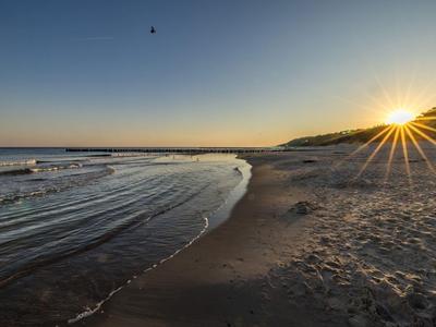 Západ slunce na pláži s jemnými vlnami a čistou oblohou.
