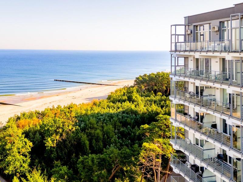 Pohled na hotel s balkony vedle lesa a pláže u moře