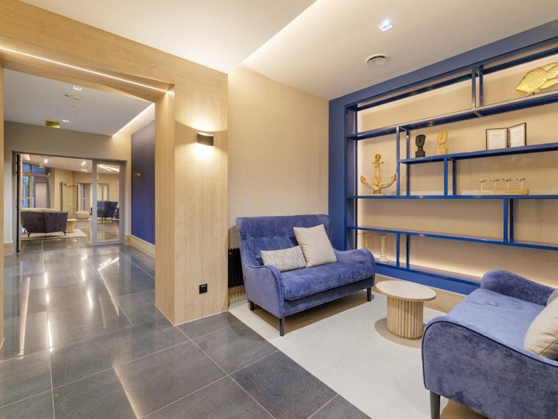 Moderní hotelová chodba s modrými pohovkami a osvětlenými policemi.