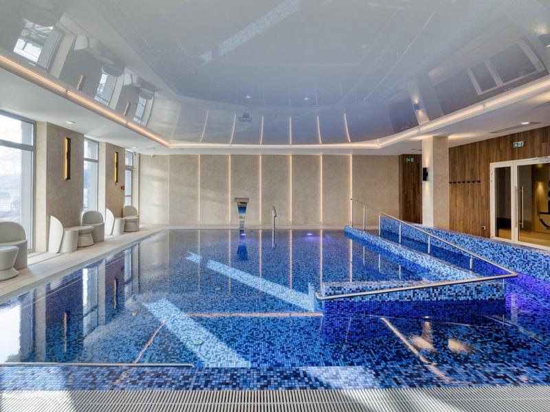 Vnitřní bazén s modrými vzorovanými dlaždicemi, posezením a přirozeným světlem z oken.