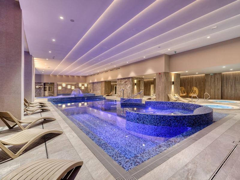 Moderní vnitřní bazén s integrovaným vířivým bazénem a lehátky v hotelu.