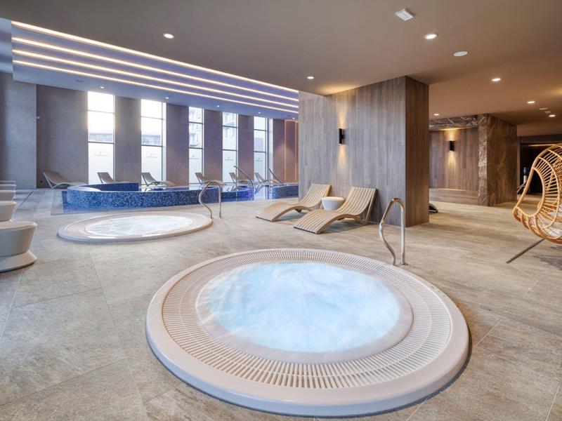 Moderní lázně s vířivkou, lehátky a bazénem v světlé místnosti.