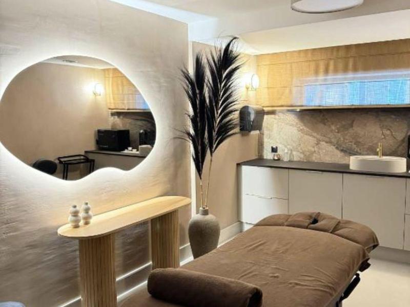 Moderní wellness místnost s masážním stolem, kulatým zrcadlem a stylovým osvětlením.