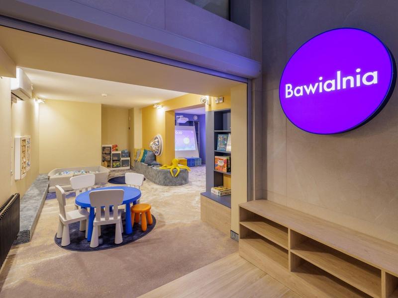 Světla herna pro děti s malými stoly, židlemi a hračkami v hotelové části.