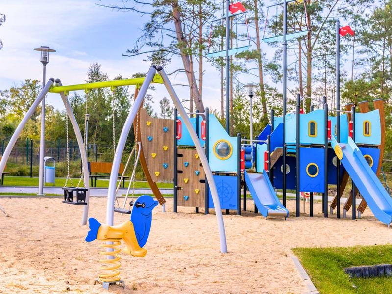 Moderní hřiště s klouzačkou, houpačkami a pískovištěm v parku.