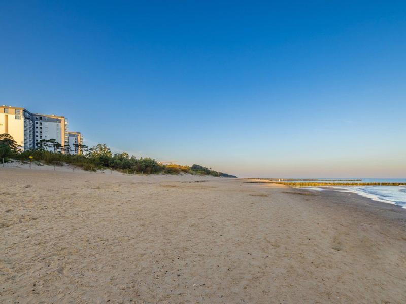 Rozsáhlá písečná pláž s několika budovami vlevo a jasně modrou oblohou.