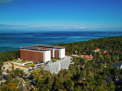 Großes Hotelgebäude nahe der Küste, umgeben von Bäumen und Meer im Hintergrund.