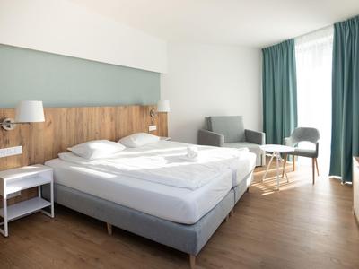 Modern eingerichtetes Hotelzimmer mit Doppelbett, Sitzbereich und großen Fenstern mit Vorhängen.