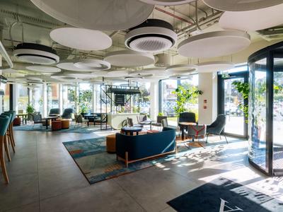 Heller Hotellobby mit moderner Einrichtung, großen Fenstern und Pflanzen.