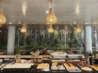 Buffet mit verschiedenen Speisen und Kuchen vor einer Wald-Wanddekoration in einem Hotelrestaurant.