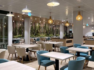 Modernes Restaurant mit weißen Tischen, blauen und beigen Stühlen sowie Pendelleuchten.