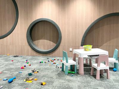 Kinderspielzimmer mit buntem Spielzeug auf dem Boden und kleinen Tischen mit Stühlen vor Holzpaneelen.