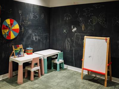 Kinder-Spielecke mit zwei kleinen Tischen, Stühlen, Tafel und Spielsachen in einem Hotelzimmer.