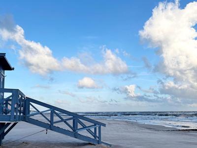 Blauer Strandhaus mit Treppe am Sandstrand unter blauem Himmel mit Wolken.
