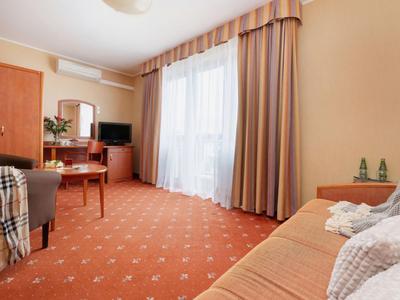 Gemütliches Hotelzimmer mit Teppichboden, Gardinen und einfacher Möblierung.