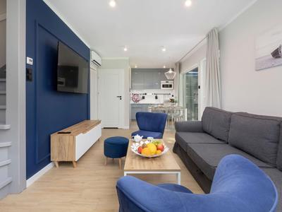 Modern eingerichtetes Wohnzimmer mit grauem Sofa, blauem Sessel und kleiner Küche im Hintergrund.