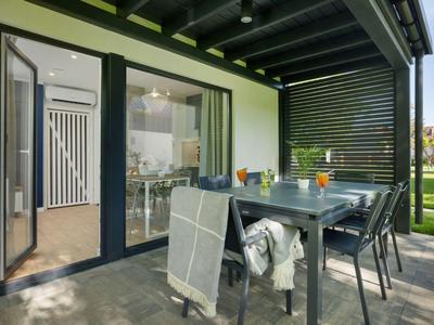 Moderner Gartenbereich mit Terrasse, Esstisch und Stühlen vor großen Glastüren zu einem Haus.