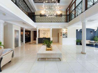 Helle Hotellobby mit modernem Mobiliar, großem Teppich und Balkon mit dekorativem Geländer.