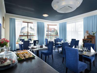 Eleganter Speisesaal mit blauen Stühlen und großen Fenstern, heller Tageslichtumgebung.