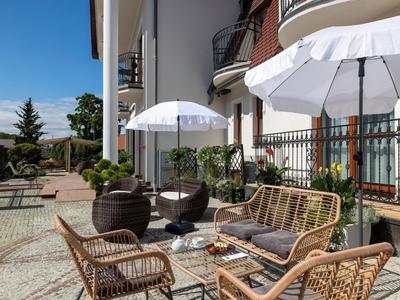 Terrasse mit Rattanmöbeln und Sonnenschirmen vor einem Hotel bei sonnigem Wetter.