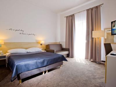 Helles Hotelzimmer mit Doppelbett, Sofa, Vorhängen und Wanddekoration im modernen Stil.