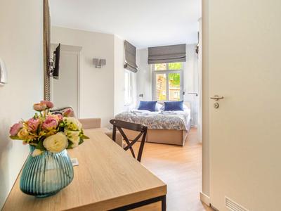 Helles Hotelzimmer mit Schreibtisch, Stuhl und Blumenstrauß vor einem gemütlichen Bett.