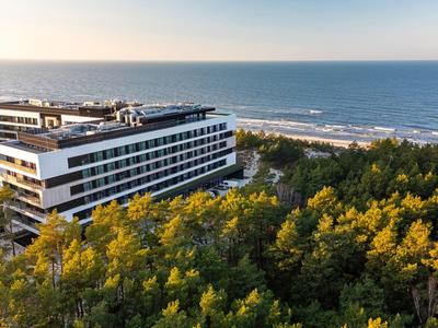 Hotel moderno con techo plano junto al mar, rodeado de denso bosque verde.