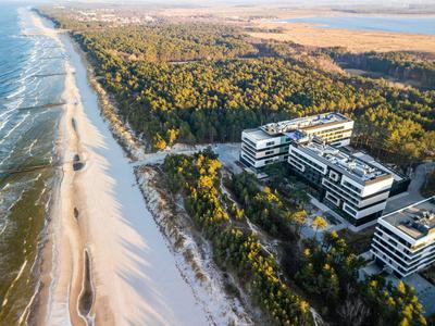 Edificios modernos de hotel en el borde del bosque cerca de una larga playa de arena y el mar.