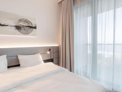 Habitación de hotel moderna con cama grande, luz suave y ventanas de piso a techo con cortinas.