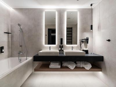 Baño moderno de hotel con dos lavabos, espejos iluminados y bañera.