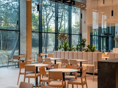 Restaurante moderno y luminoso con grandes ventanales y muebles de madera con vista a la naturaleza.