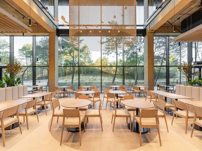 Restaurante moderno y luminoso con diseño de madera y vidrio con vista al entorno verde.