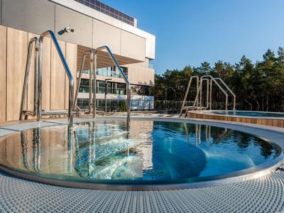Jacuzzi redondo con chorros de agua en una terraza frente a un edificio moderno y árboles.