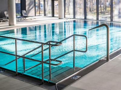 Piscina interior con agua clara, paredes de vidrio y barandillas metálicas en un hotel moderno.
