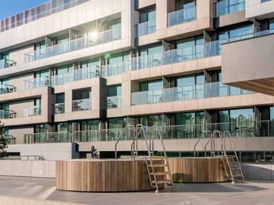 Piscina exterior moderna con tinas redondas de madera frente a un hotel con balcones.