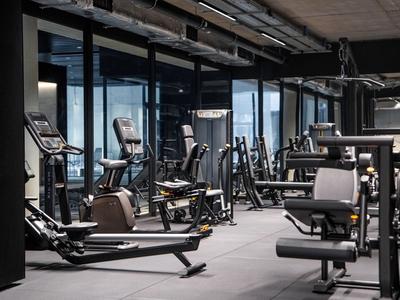Gimnasio moderno con varias máquinas de entrenamiento y grandes ventanas con vistas a la ciudad.
