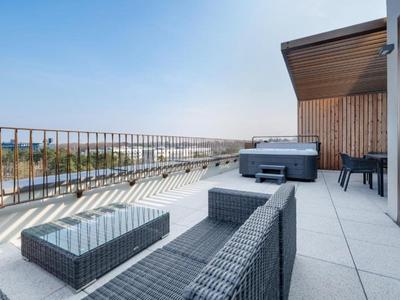 Moderní balkon s lounge nábytkem a vířivkou s výhledem na město pod jasnou oblohou.